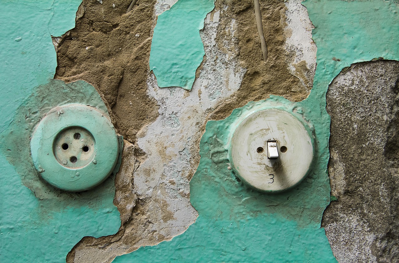 Old round light switch and power outlet on flaking green-painted plaster